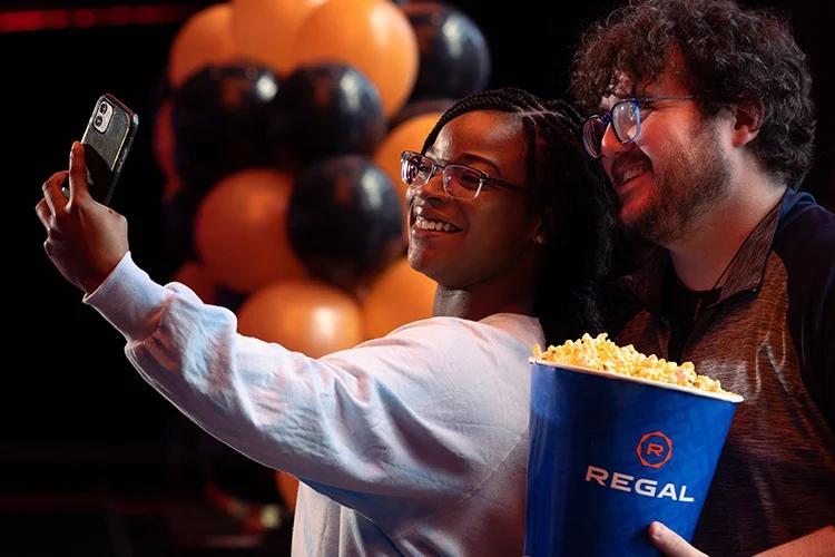 Couple taking a selfie with bucket of popcorn.