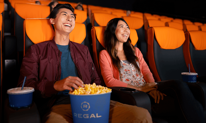 Happy couple laughs while watching a movie and eating popcorn.