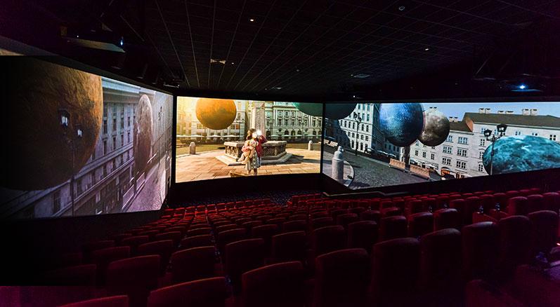 little girl with a teddy bear watchings planets fly through the street in a ScreenX theatre