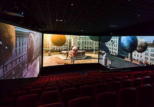 little girl with a teddy bear watchings planets fly through the street in a ScreenX theatre