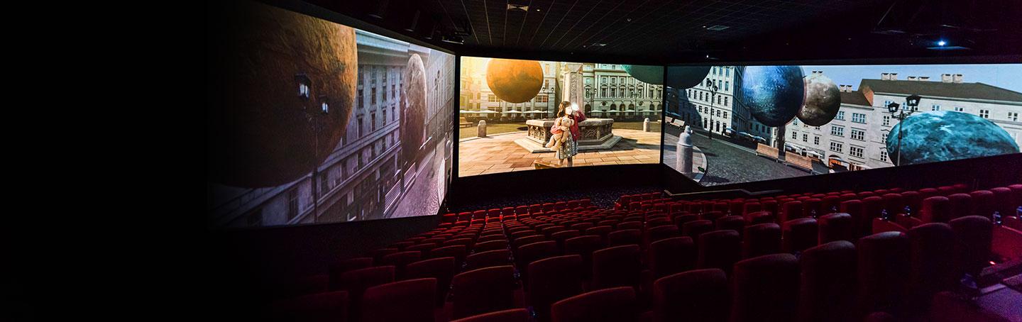 little girl with a teddy bear watchings planets fly through the street in a ScreenX theatre